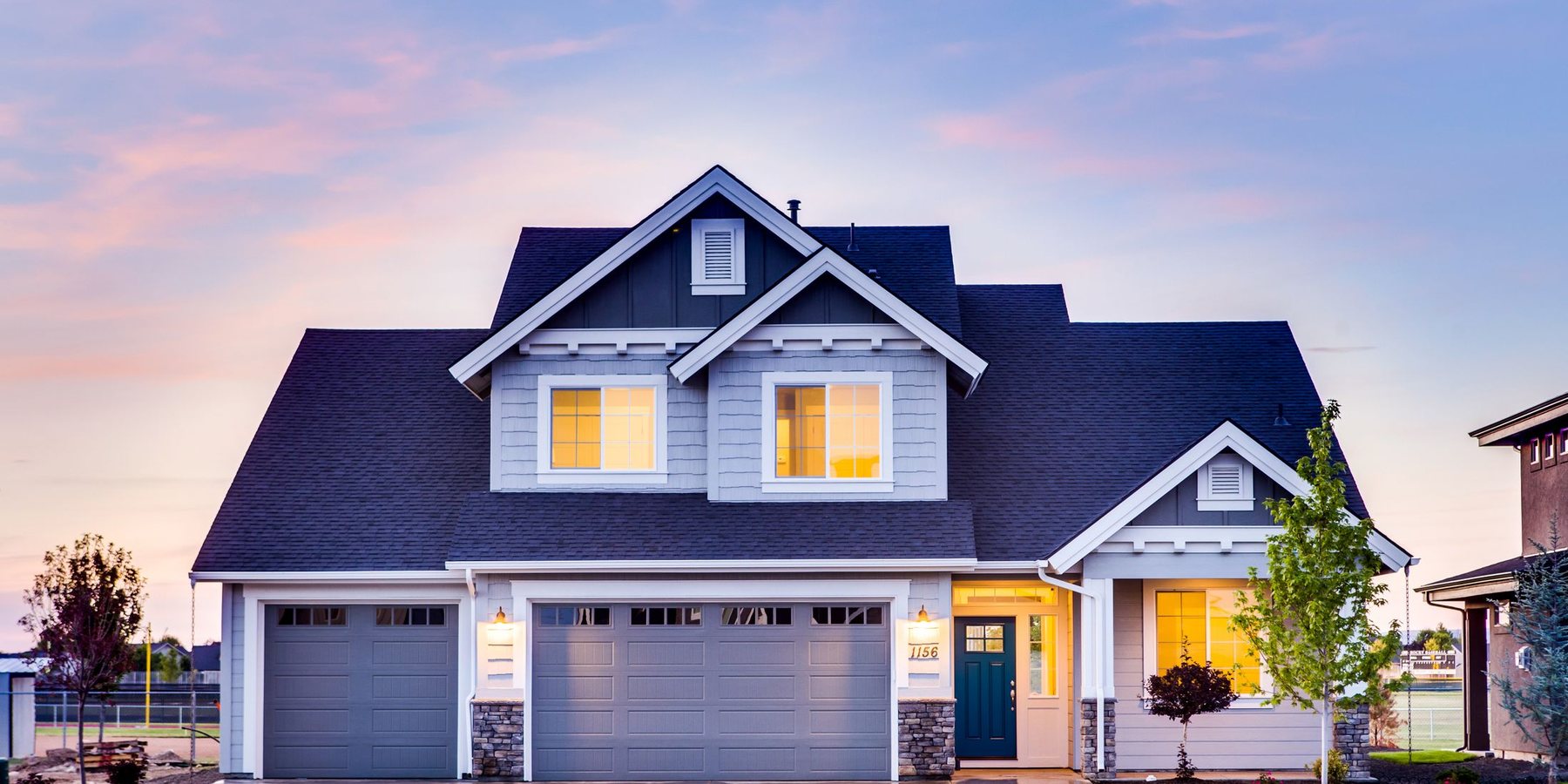 A two story house at dusk with warm light in the upstairs windows, a three car garage and a wet driveway.