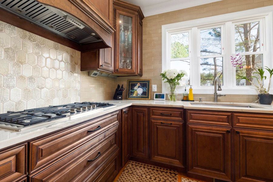 A kitchen counter run with a gas cooktop, stone tile backsplash, quartz counters and a window over the sink.