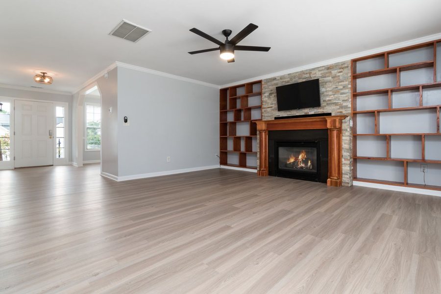 The same family room photographed from the opposite corner, showing the front door, the fireplace and the new floor running through.