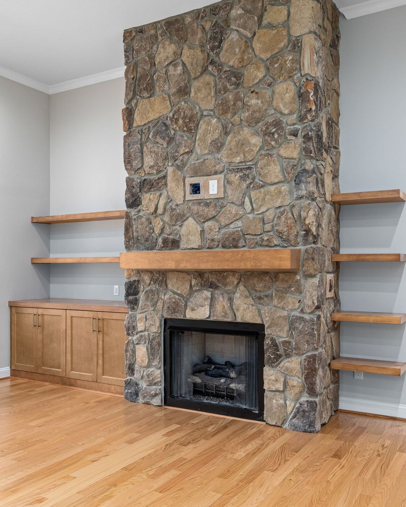 A floor to ceiling stone fireplace with a thick wooden mantel, floating wood shelves either side and low built-in cabinets.