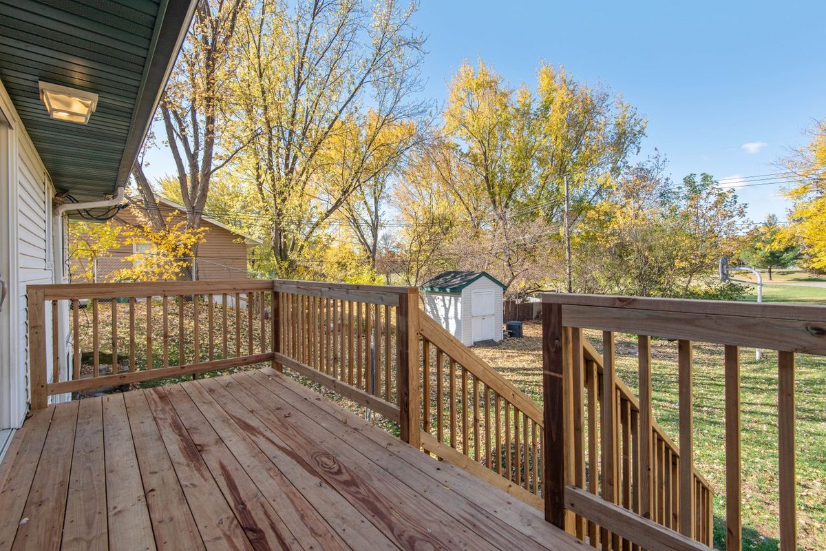 A newly built pressure treated deck with square balusters, looking out over a back yard with yellow fall trees and a storage shed.