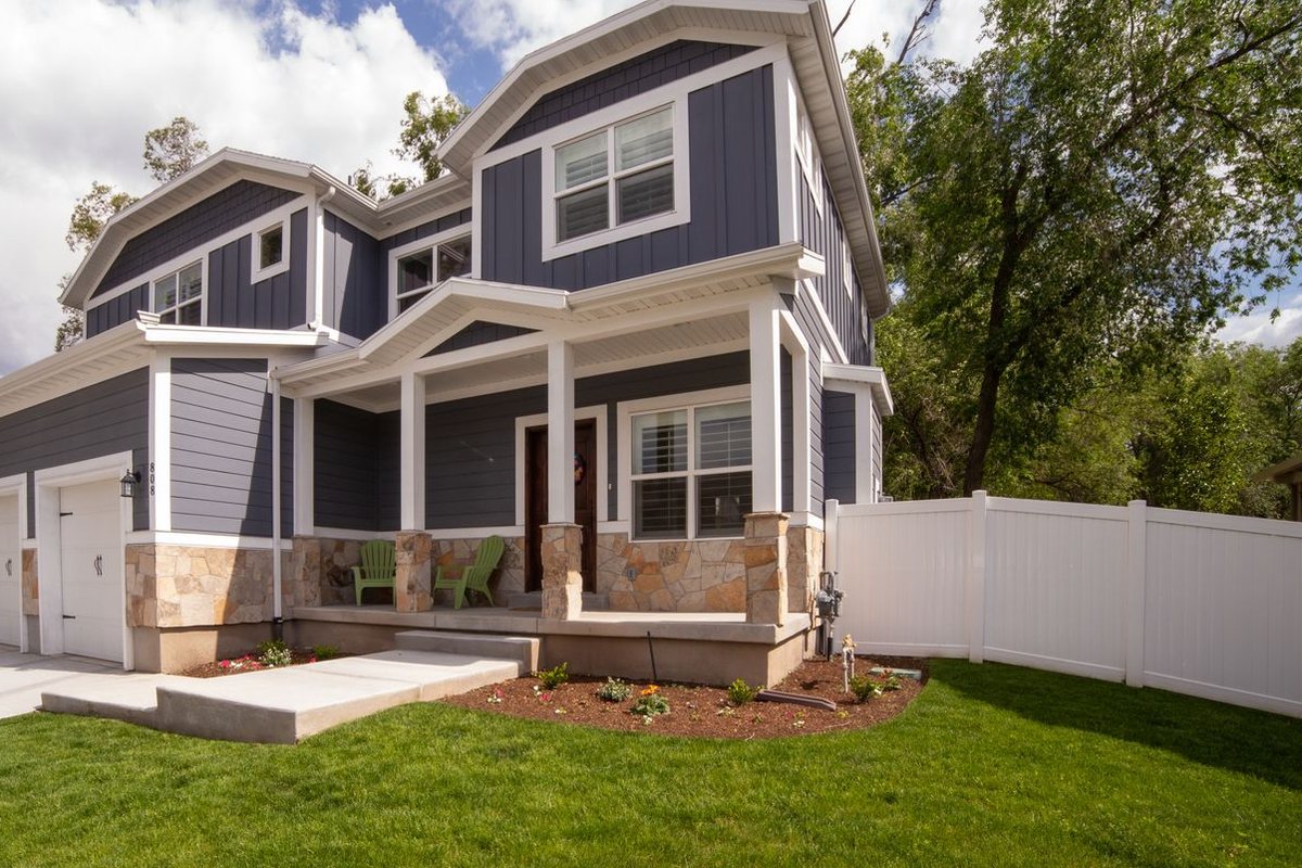 A two story house with navy lap and board and batten siding, white trim, stone skirting and a covered front porch.