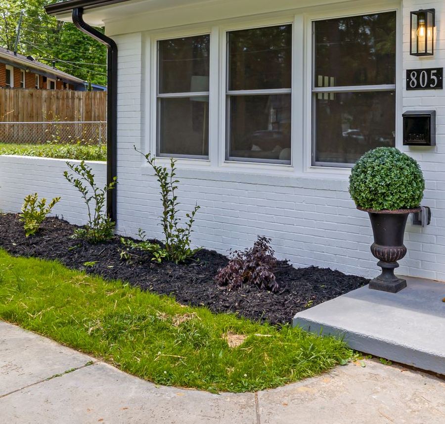 A walkway beside a freshly mulched bed with a boxwood in a stone urn.