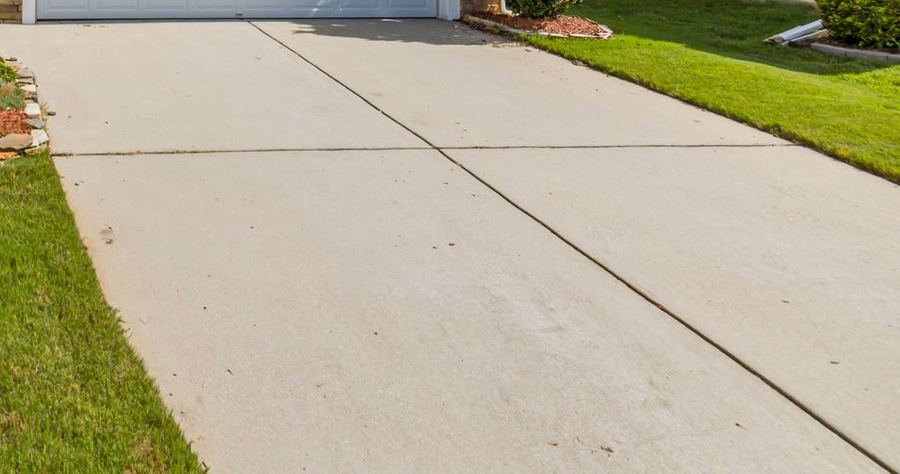 A wide concrete driveway running past a cut lawn.