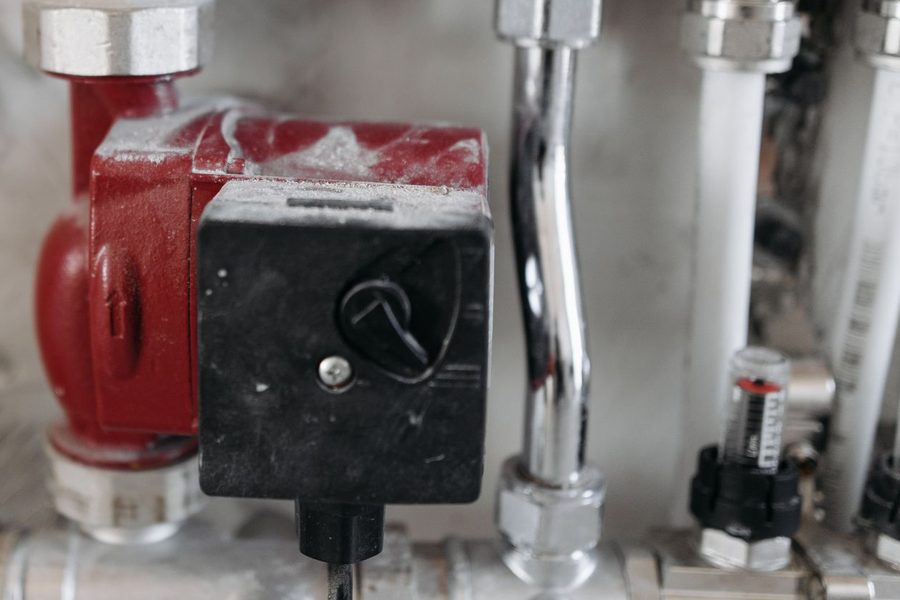 A red circulator pump and chrome unions on a basement heating manifold.