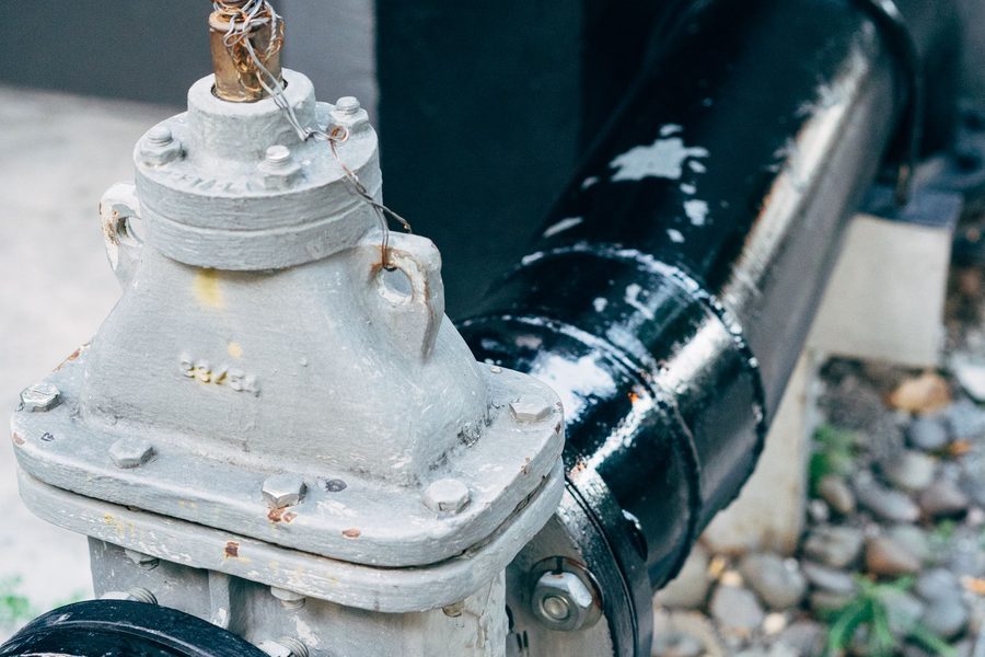 A painted cast iron gate valve bolted between two sections of black pipe outside a building.