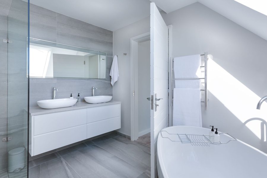 A gray and white bathroom with two vessel basins on a wall hung vanity and a freestanding tub.