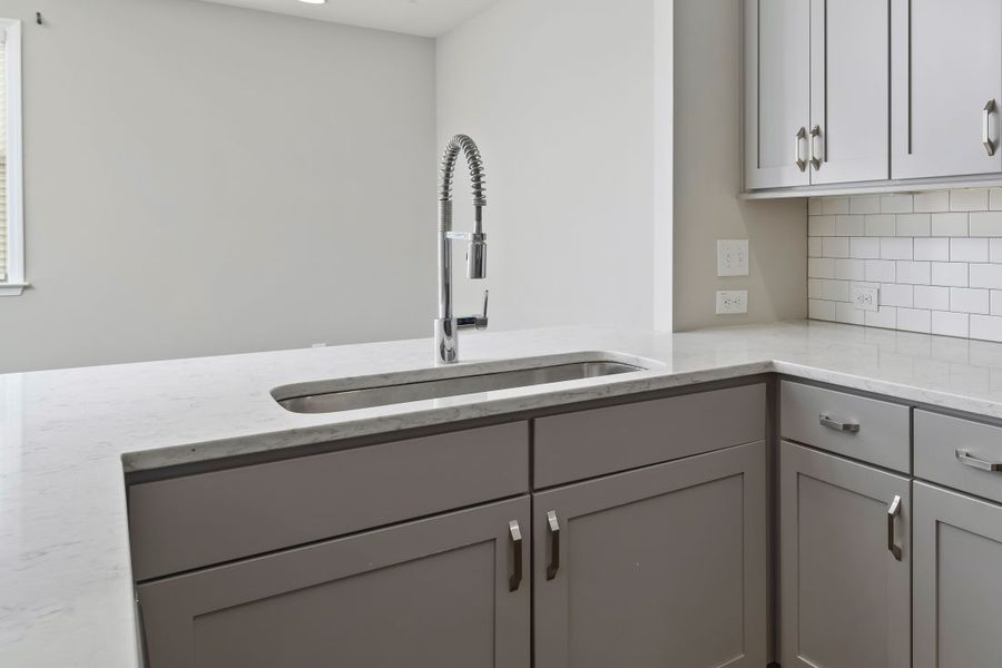 An undermount stainless kitchen sink and a chrome pull down faucet on a stone counter with gray cabinets.