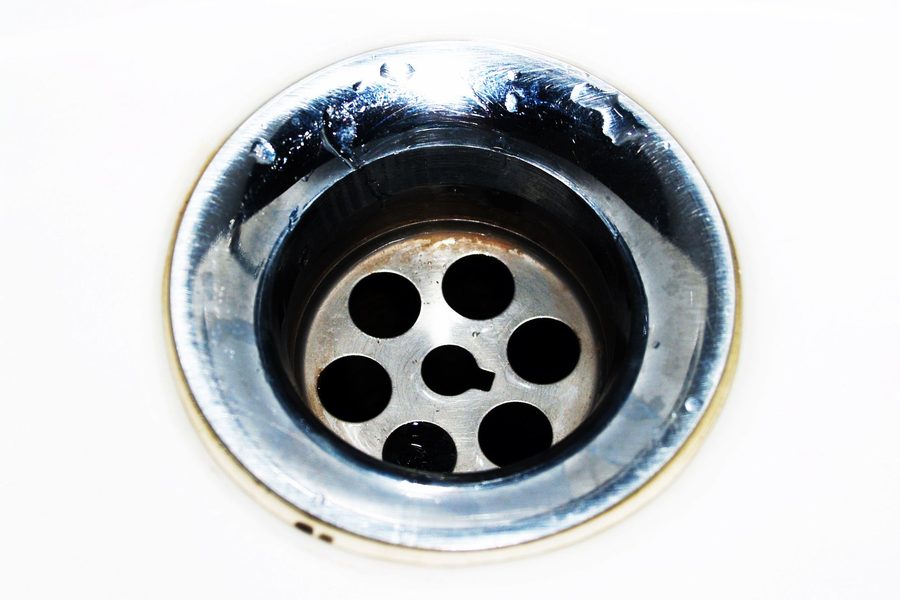 A close up of a stainless steel sink drain strainer set in a white basin.
