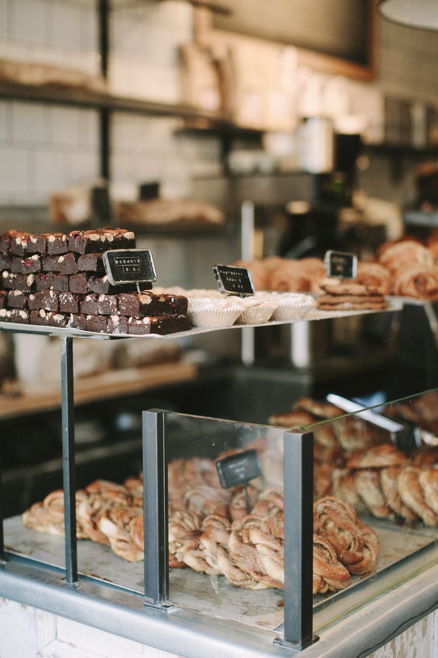 A bakery counter with stacked brownies, small cakes in paper cups, cookies and trays of cinnamon twists under glass.