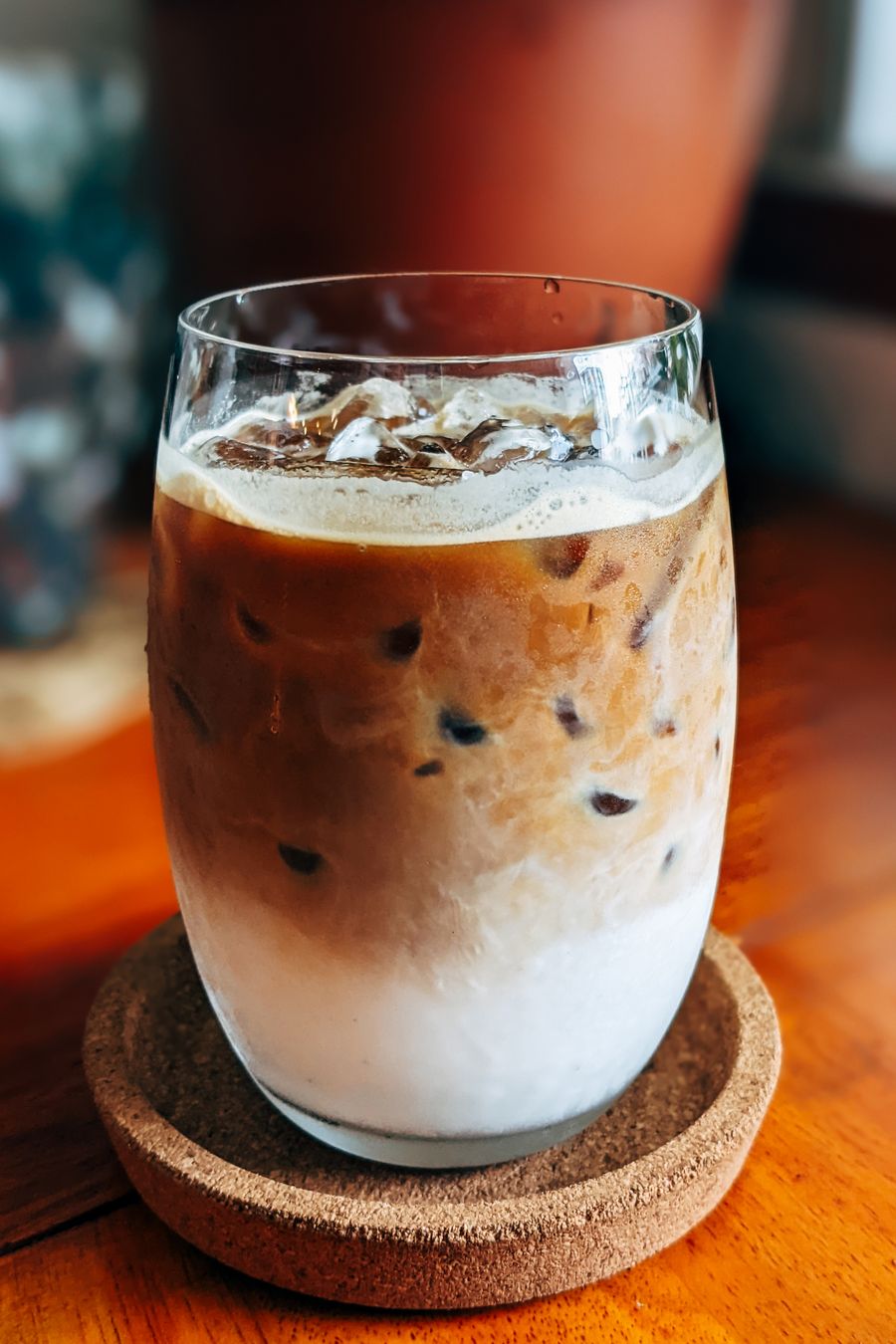 An iced latte in a rounded glass on a cork coaster, the milk settled below the coffee.