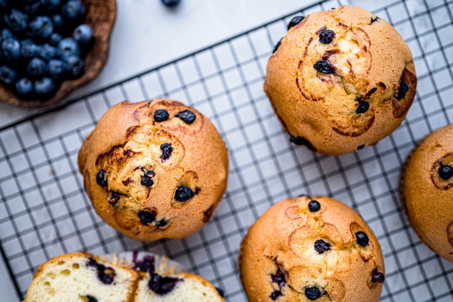 Golden blueberry muffins on a wire cooling rack with a bowl of fresh blueberries beside them.