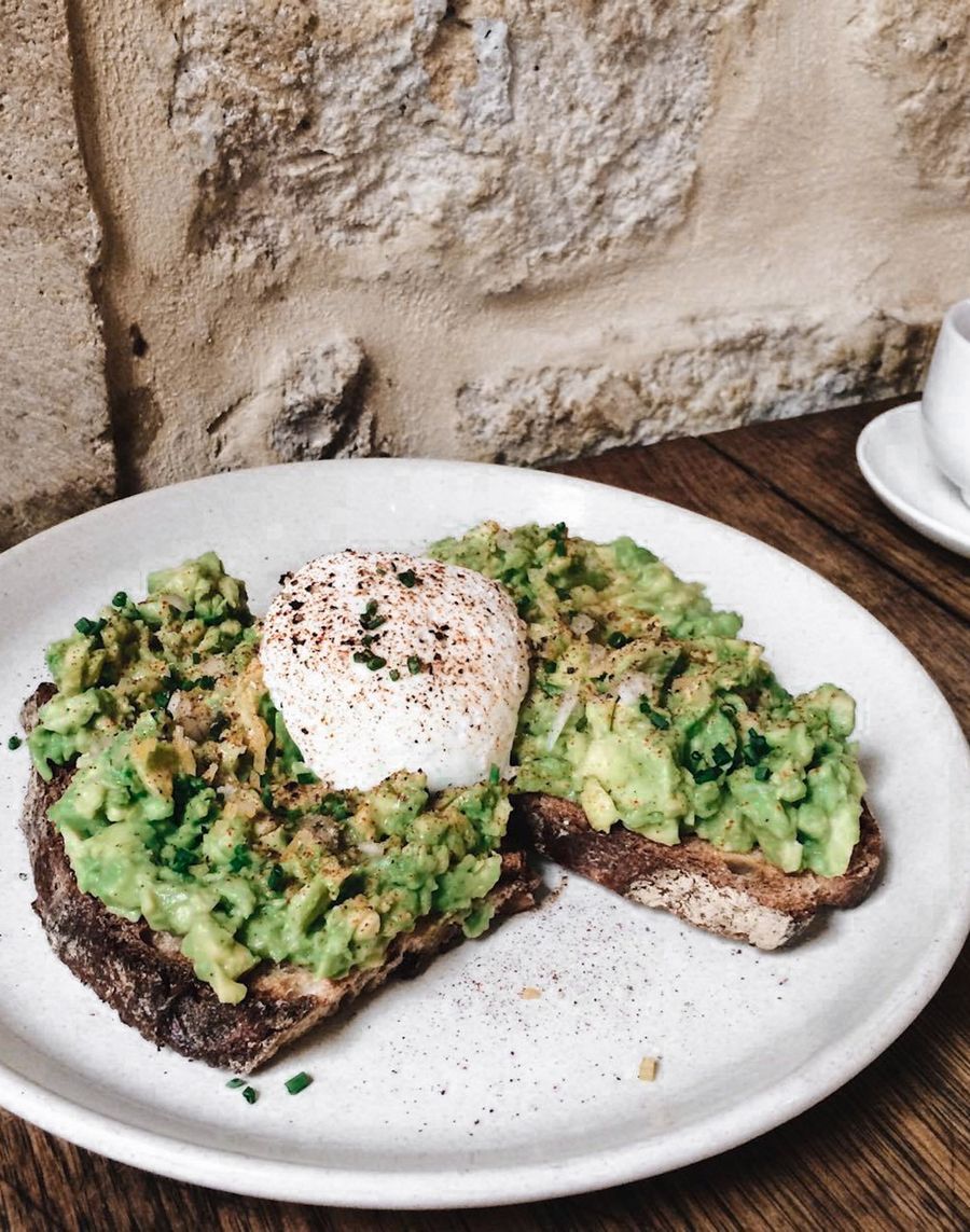 Avocado toast topped with a poached egg and chives on a speckled stoneware plate, on a dark wooden table.