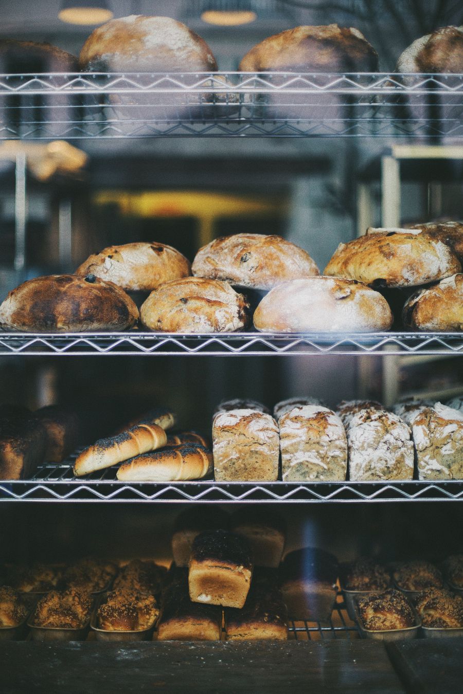 Shelves of round and tin loaves stacked on wire racks behind a bakery window.