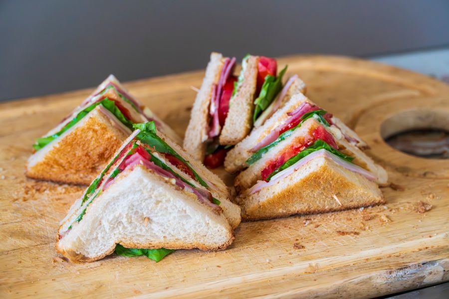 A club sandwich cut into quarters and stood up on a wooden board, layered with ham, lettuce and tomato.