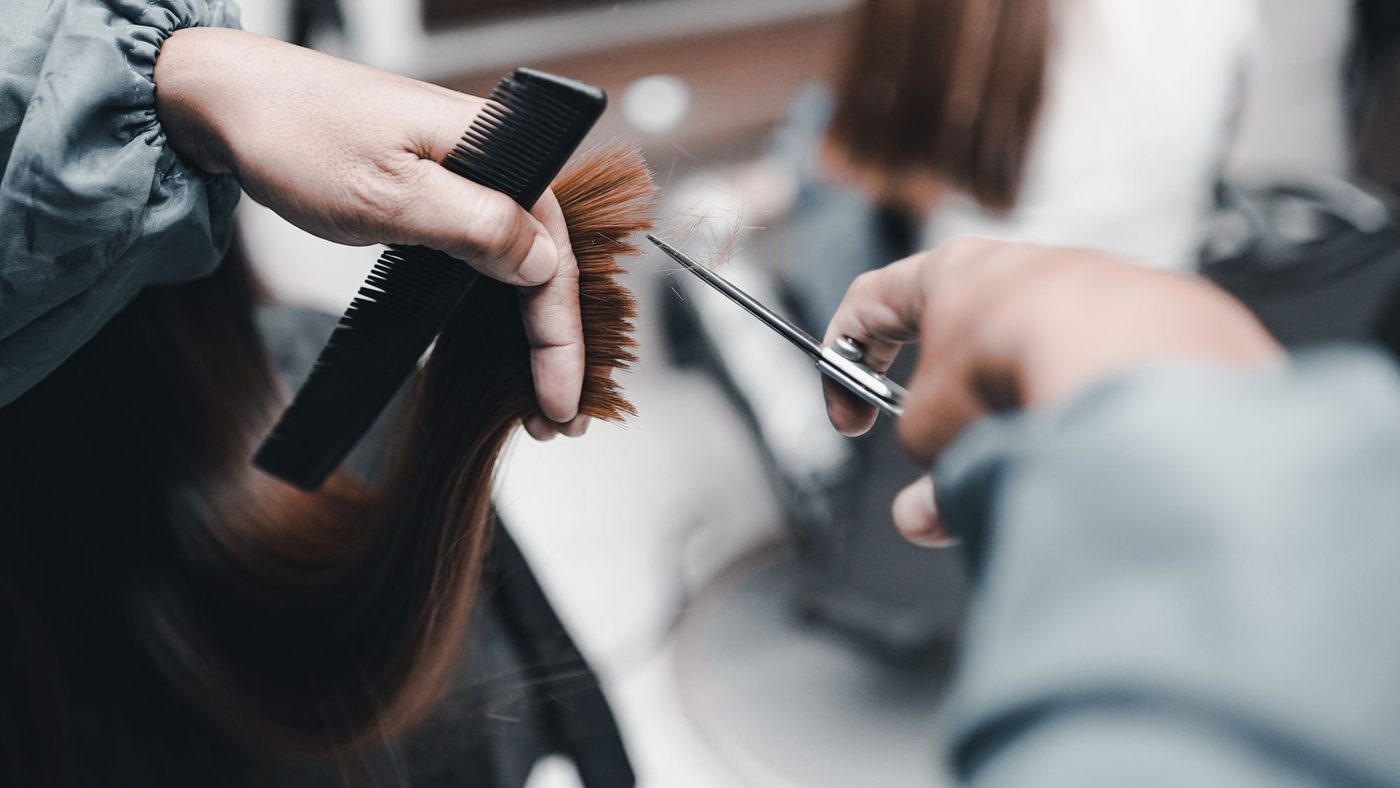 A stylist holding a section of auburn hair against a comb and cutting the ends.