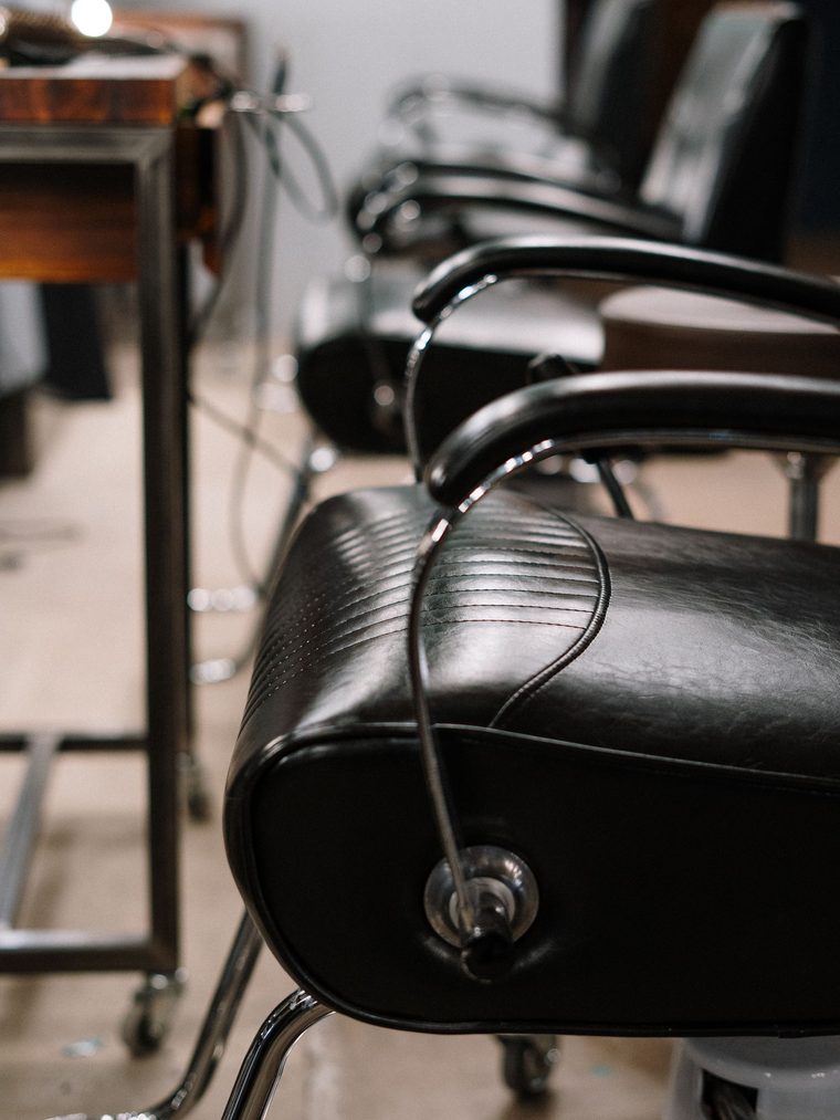 A black leather styling chair beside a wooden station with a mirror light behind it.