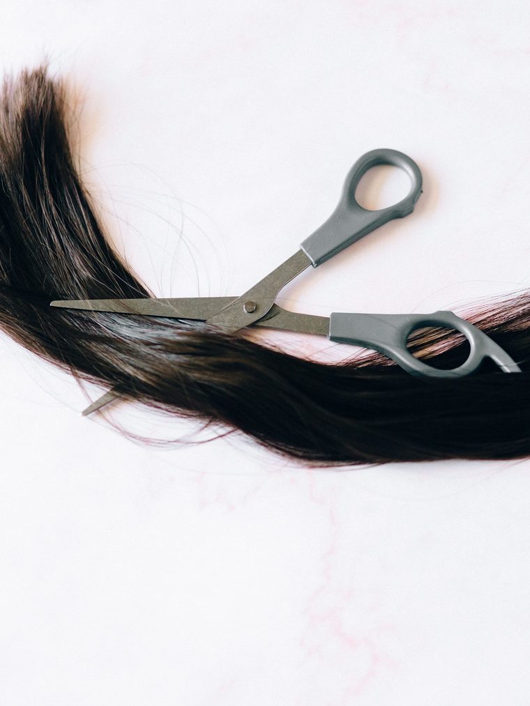 A length of dark brown hair laid across a pale surface with a pair of shears open across it.