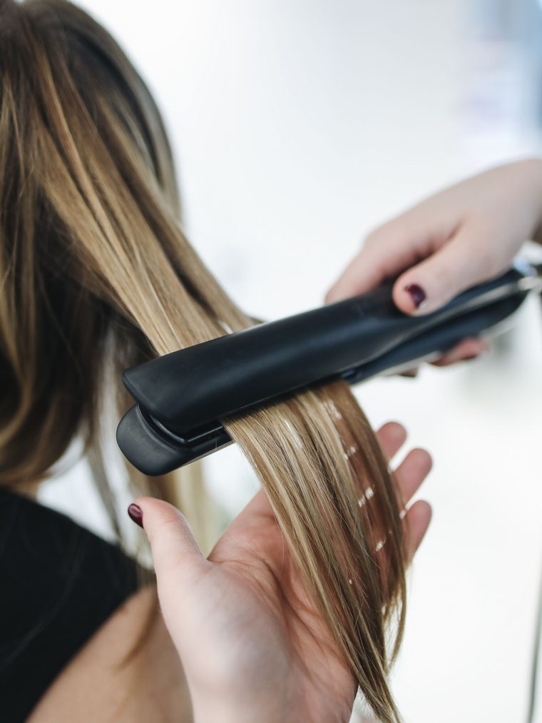 A flat iron passing over a section of blonde and brown highlighted hair.