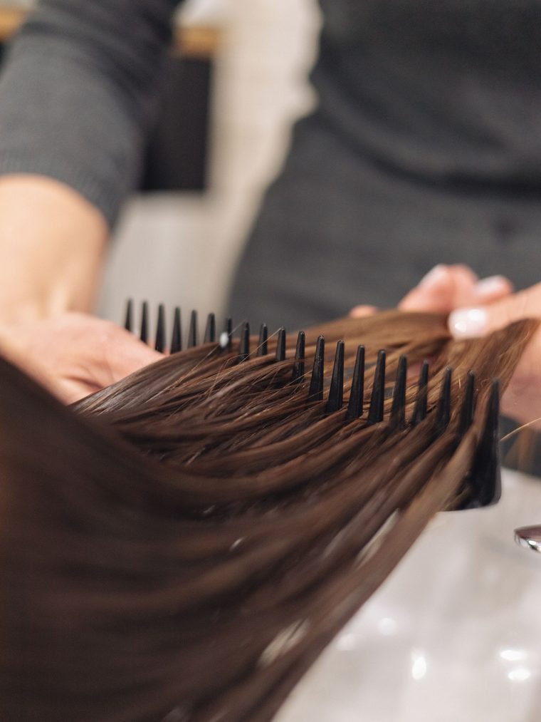 A wide tooth comb detangling long wet brown hair beside a white basin.