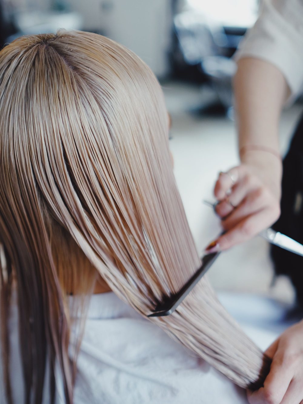 A stylist sections long blonde hair with a fine tooth comb, holding shears in the other hand.