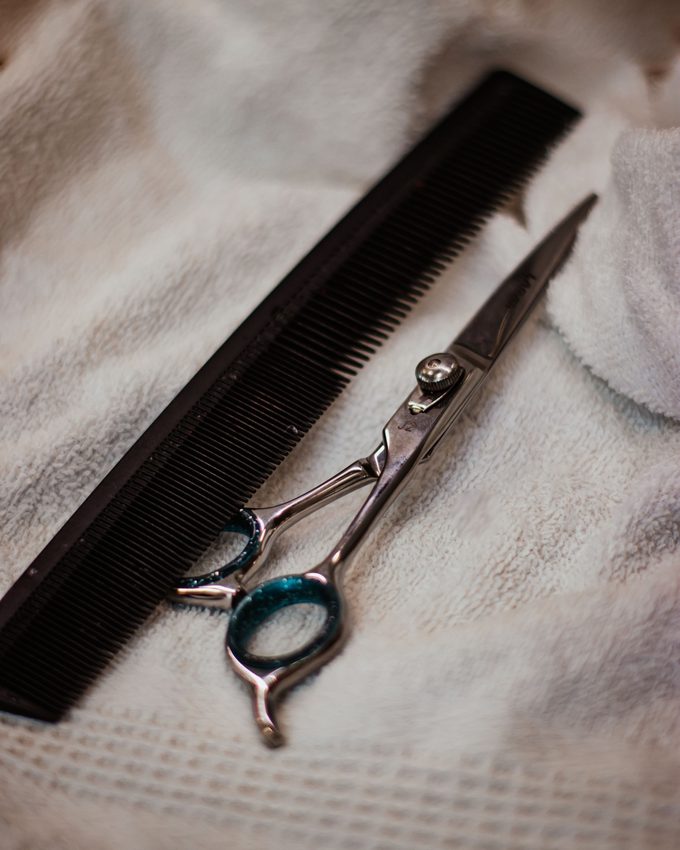 A pair of hairdressing shears and a black cutting comb resting on a cream towel.