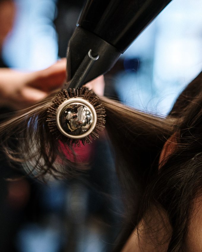 A round brush and a dryer drawing a section of dark hair straight.